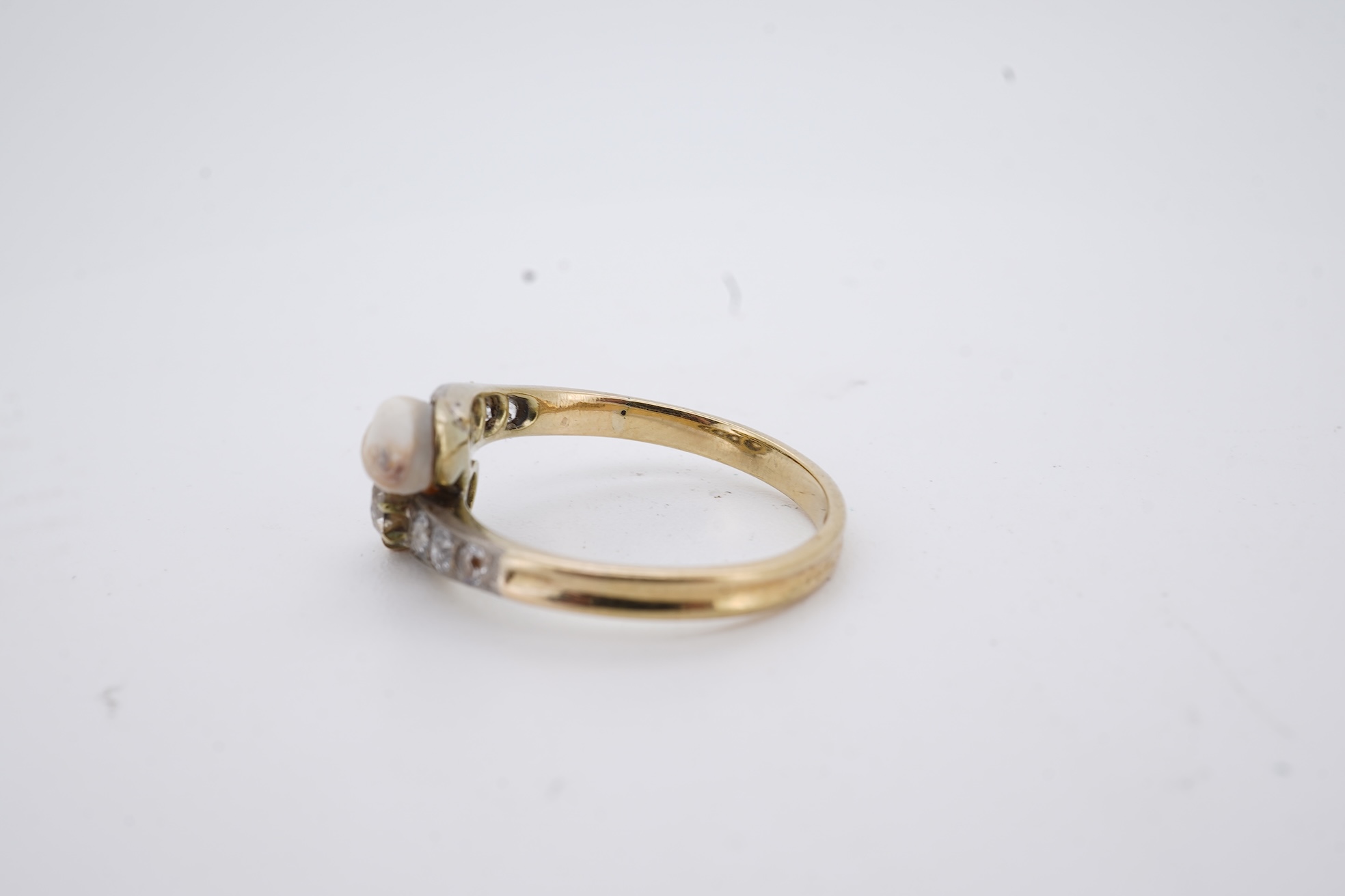 A yellow meta (stamped 18ct) cultured pearl and diamond set crossover ring, with six stone graduated diamond set shoulders, size M, gross weight 2.6 grams (pearl nacre a.f.).